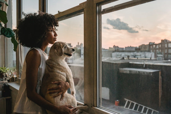 A woman cuddling her dog while standing near a window